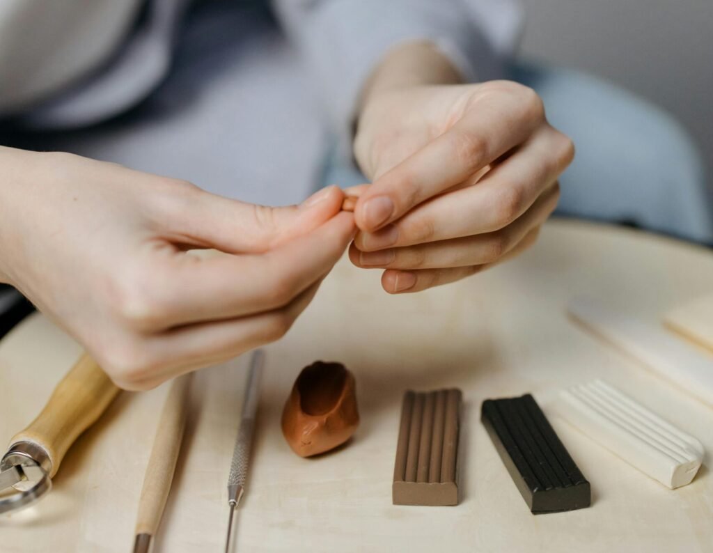 Hands shaping polymer clay in an artistic workspace with tools and materials.
