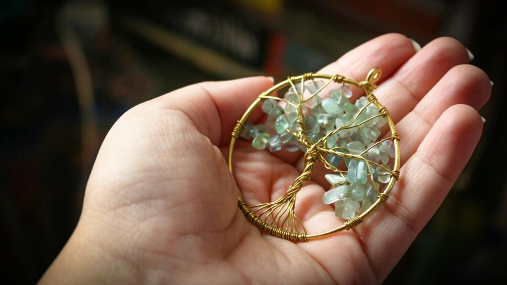 A close-up of a handmade pendant with a gemstone tree in a human hand, showcasing artistic craftsmanship.